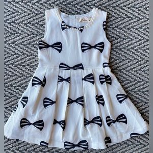 Little girls dress with a pearl lined neck line and a bow print